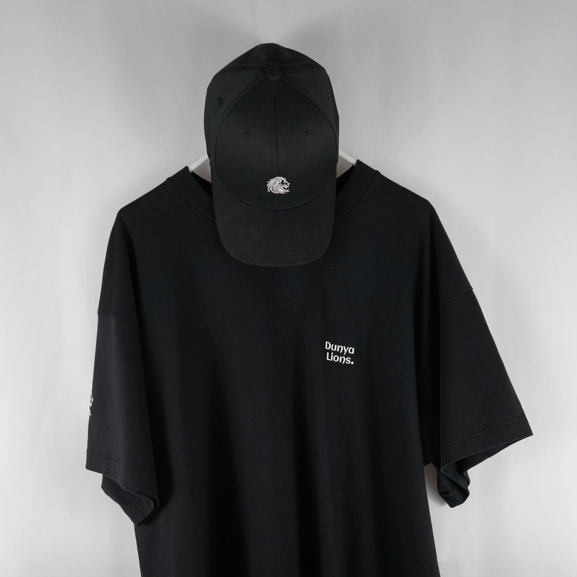 DL_Tee_Results_FrontWithCap01
Alt-Text: Front view of the Dunya Lions black t-shirt with small chest print, paired with matching black cap.