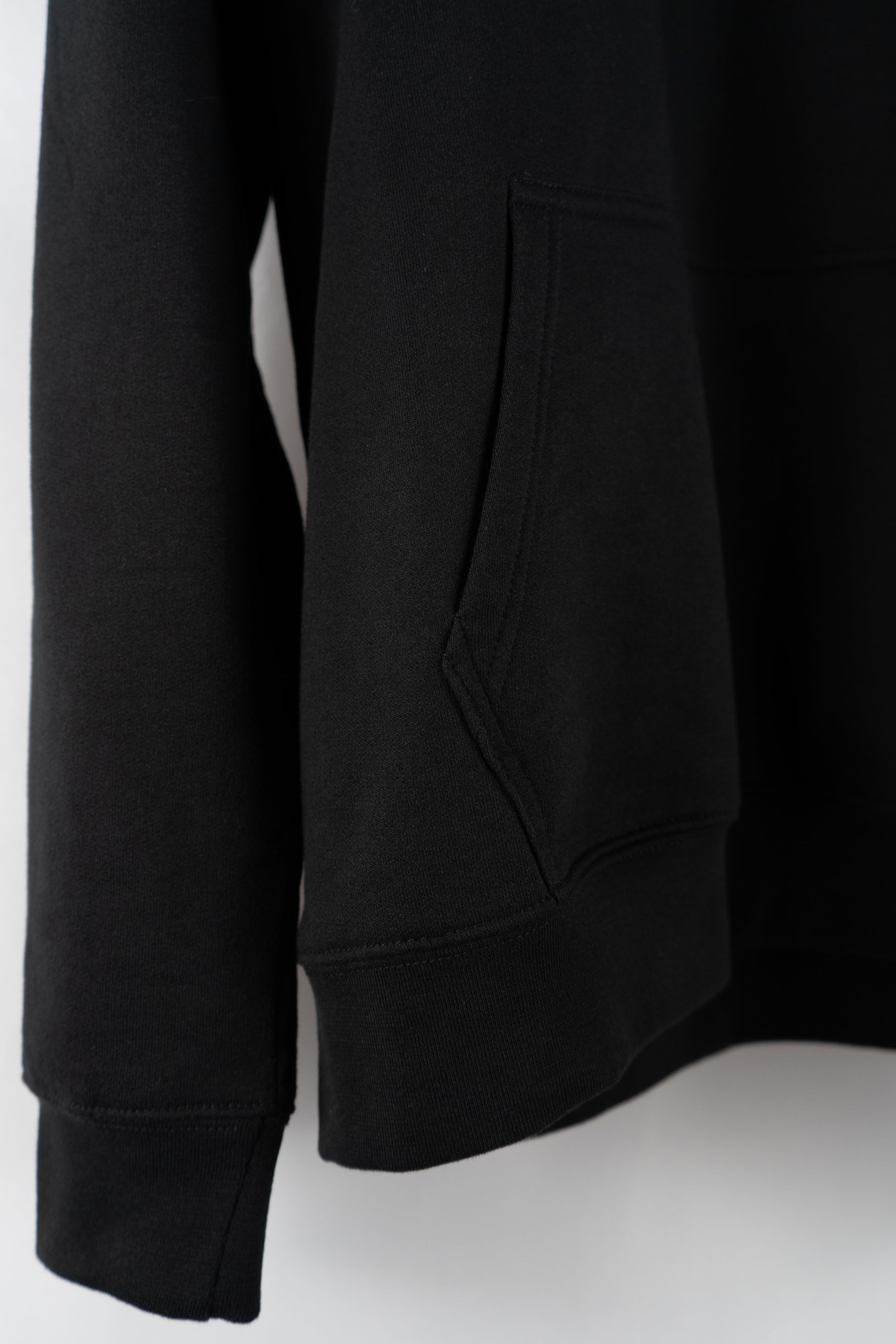 Detail shot of the front pocket and bottom hem of a black Dunya Lions hoodie, highlighting clean stitching and heavyweight fabric.
