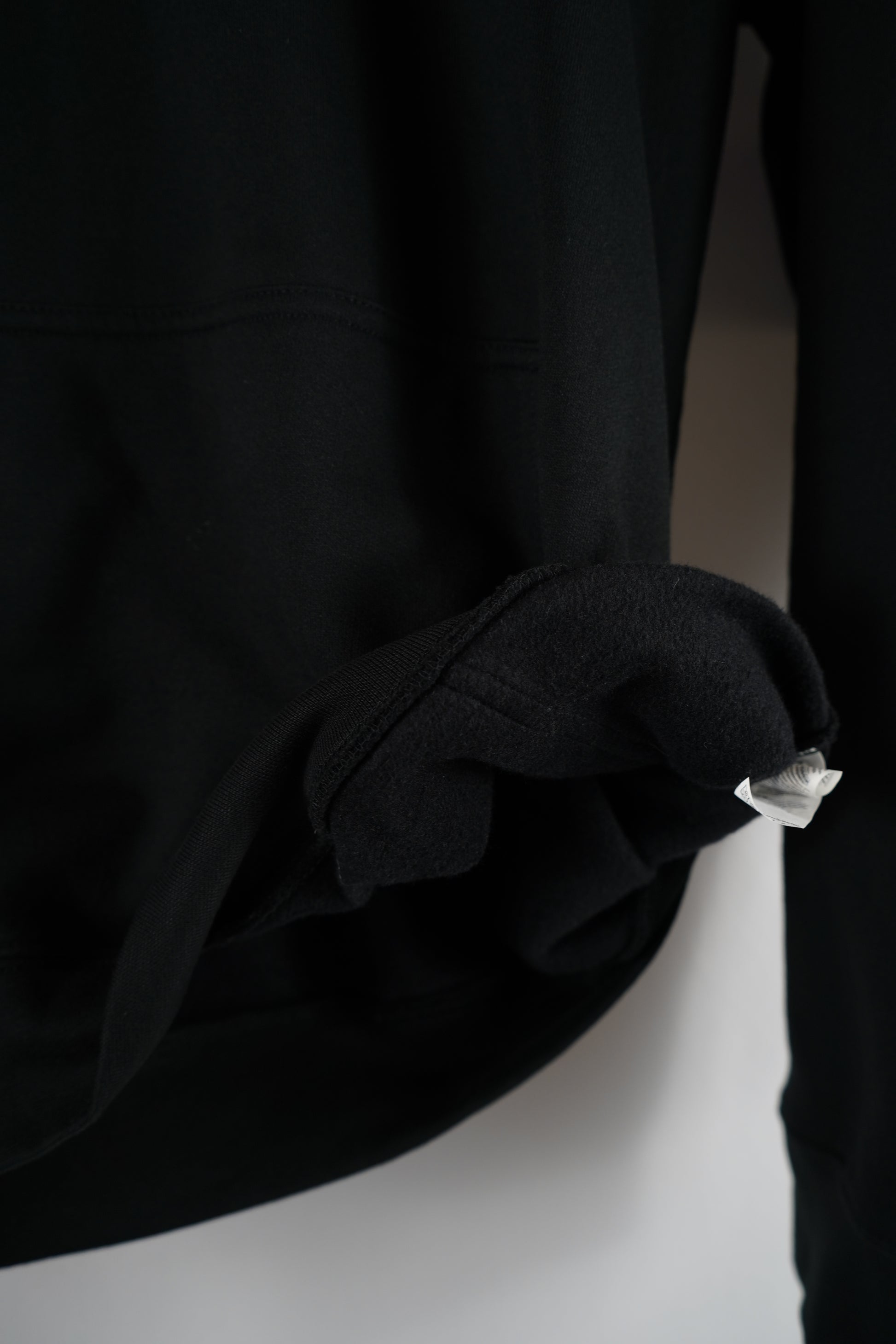 Close-up of the rolled sleeve cuff of a black Dunya Lions hoodie, showing the fabric thickness and stitching under soft light.