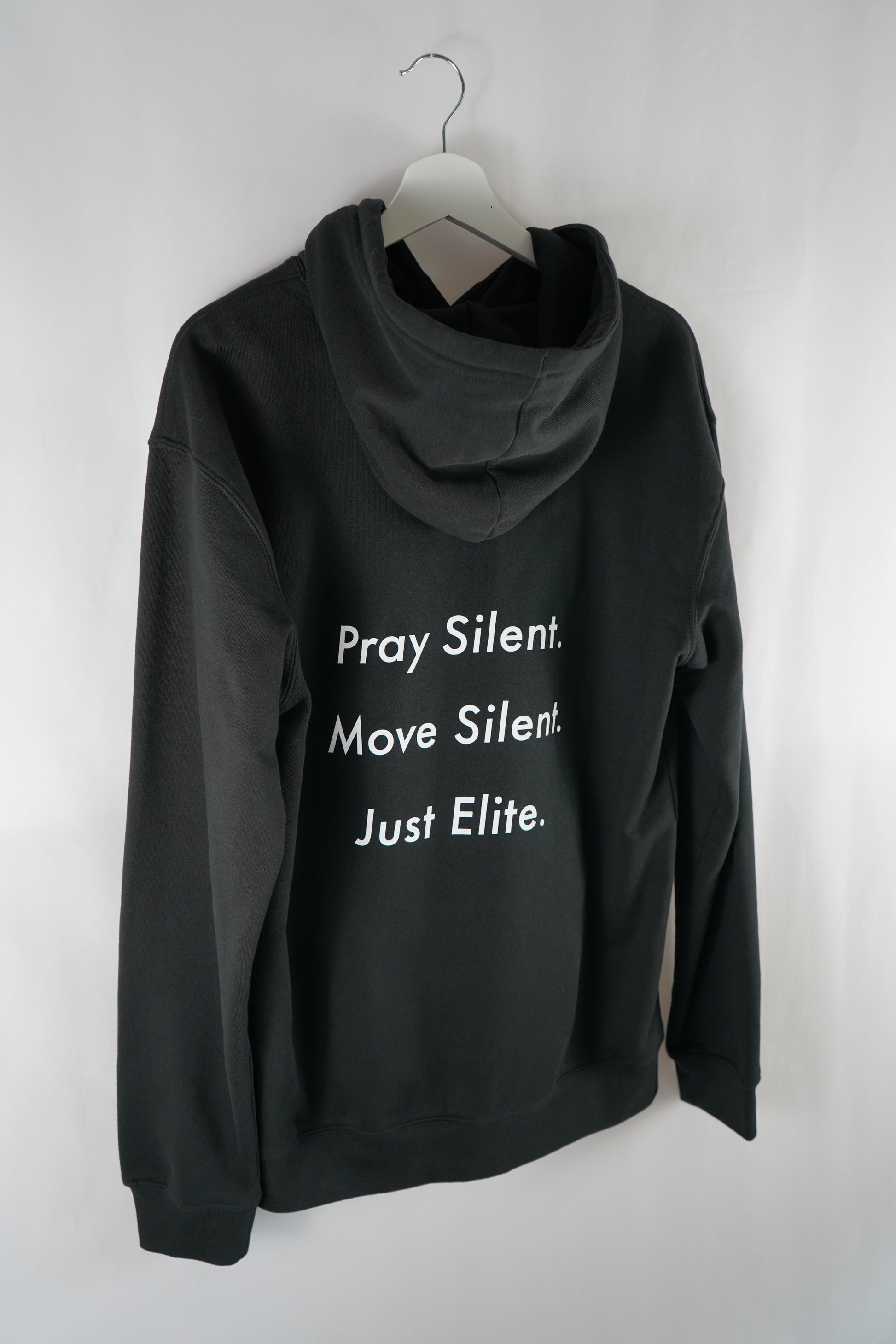 Back view of black Dunya Lions hoodie with bold white text: "Pray Silent. Move Silent. Just Elite." – hanging on a white hanger, studio-lit.
