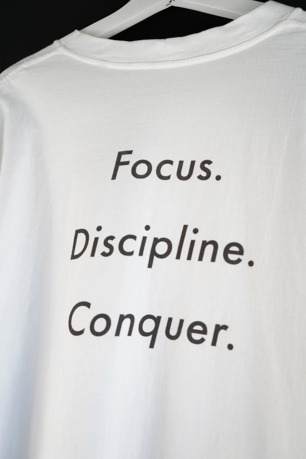 Close-up of black text “Focus. Discipline. Conquer.” printed on the back of a white oversized T-shirt.