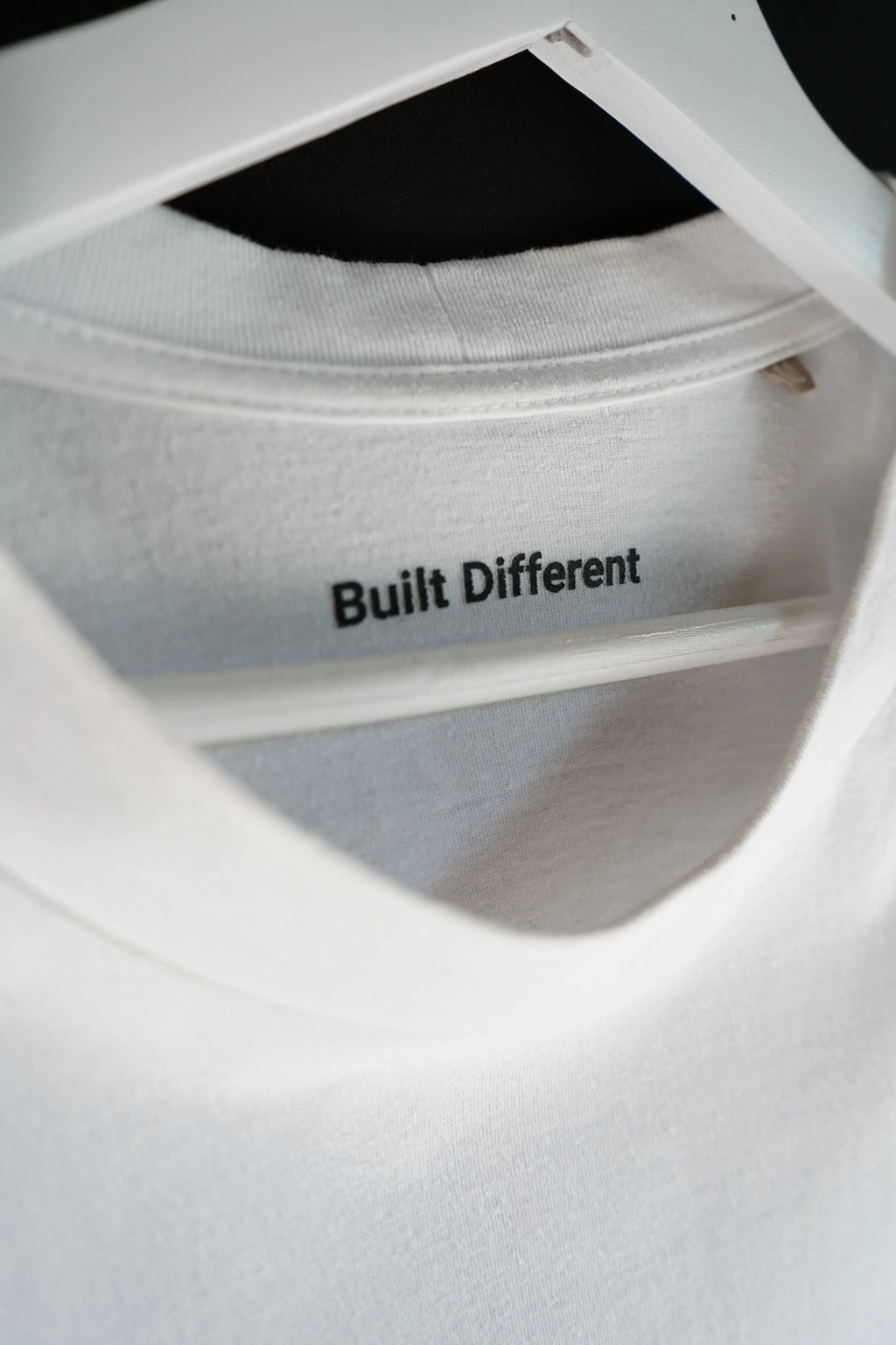 Close-up of the inside neck label reading “Built Different” in black text on a white oversized T-shirt.
