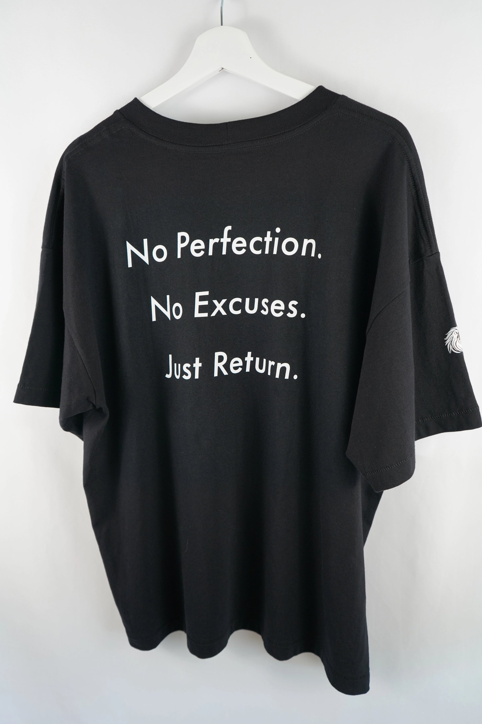Nahaufnahme des Schriftzugs „No Perfection. No Excuses. Just Return.“ auf schwarzem Shirt.