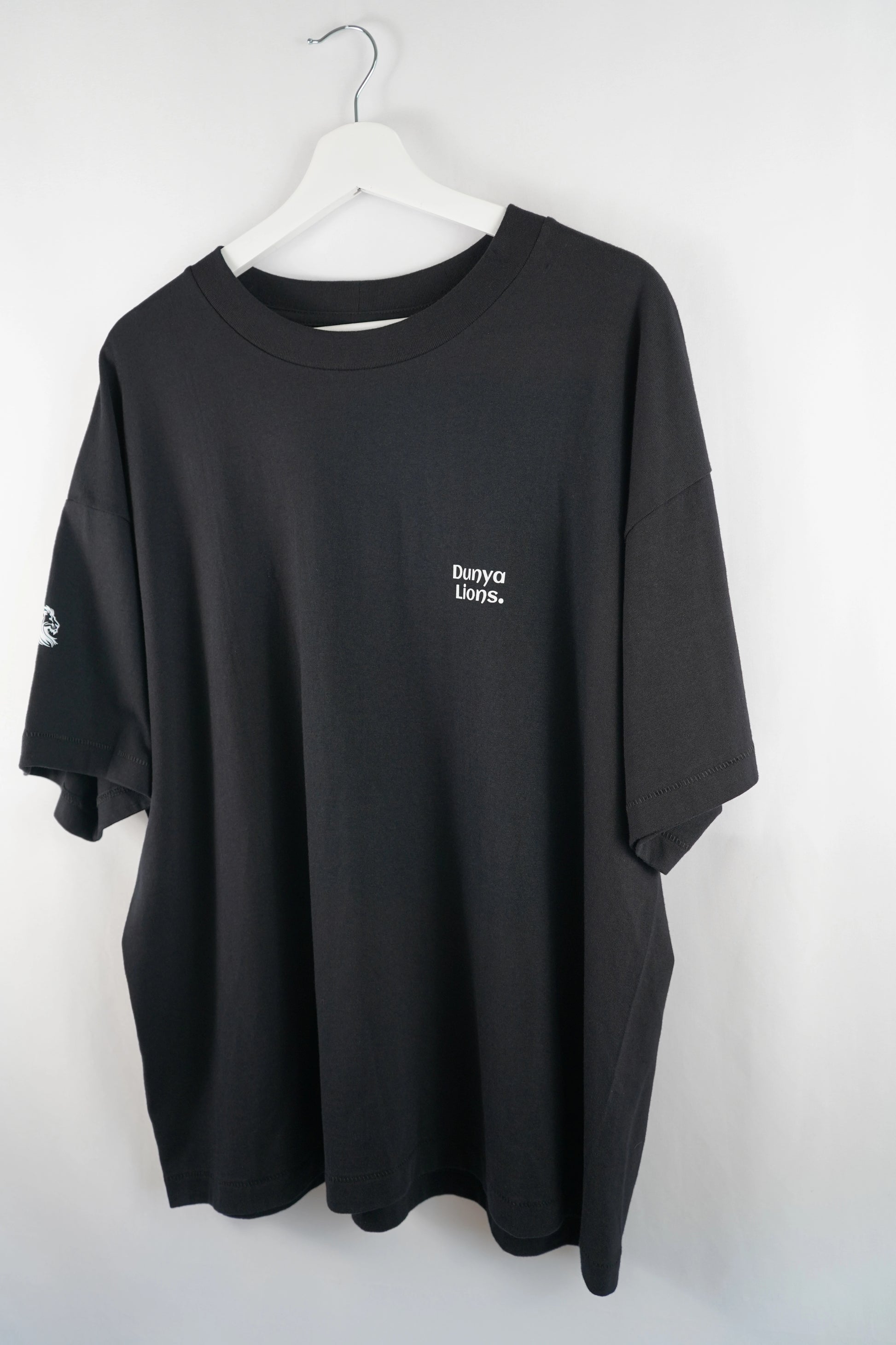 Komplettes schwarzes Dunya-Lions-Shirt mit Rückenspruch, hängend aufgenommen.