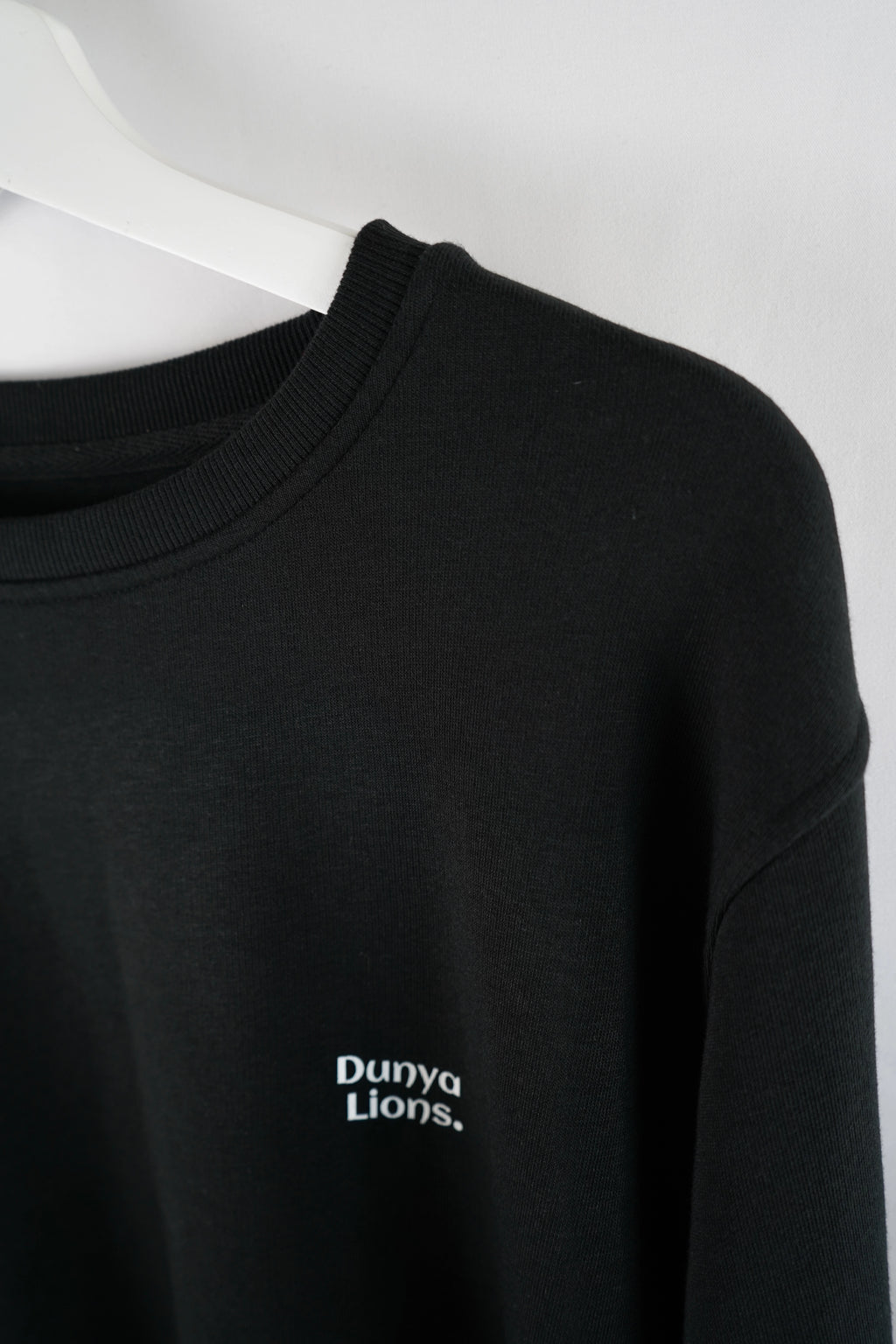 Detailaufnahme des kleinen Brustlogos „Dunya Lions.“ – ruhige Stärke auf schwarzem Stoff.