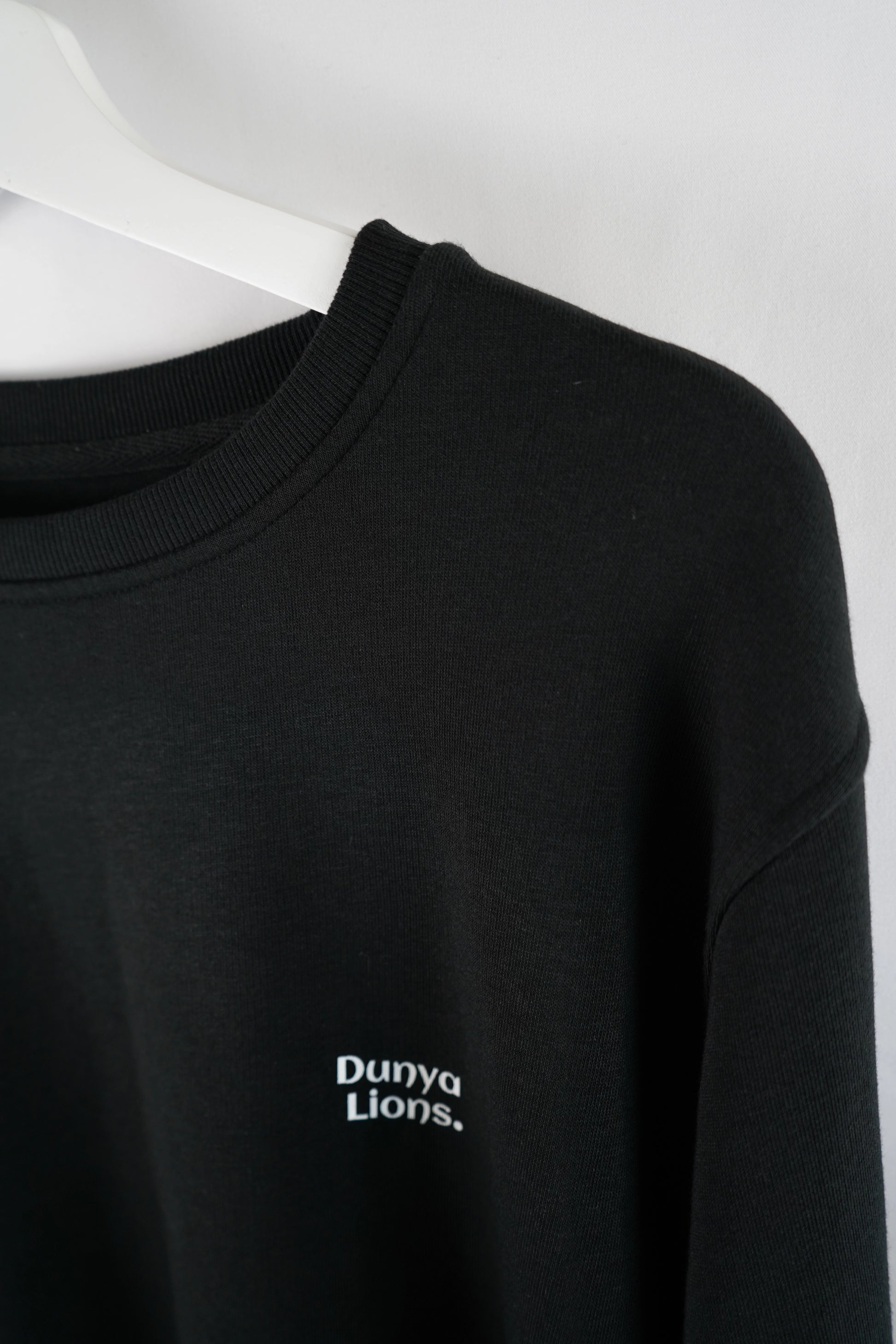 Detailaufnahme des kleinen Brustlogos „Dunya Lions.“ – ruhige Stärke auf schwarzem Stoff.