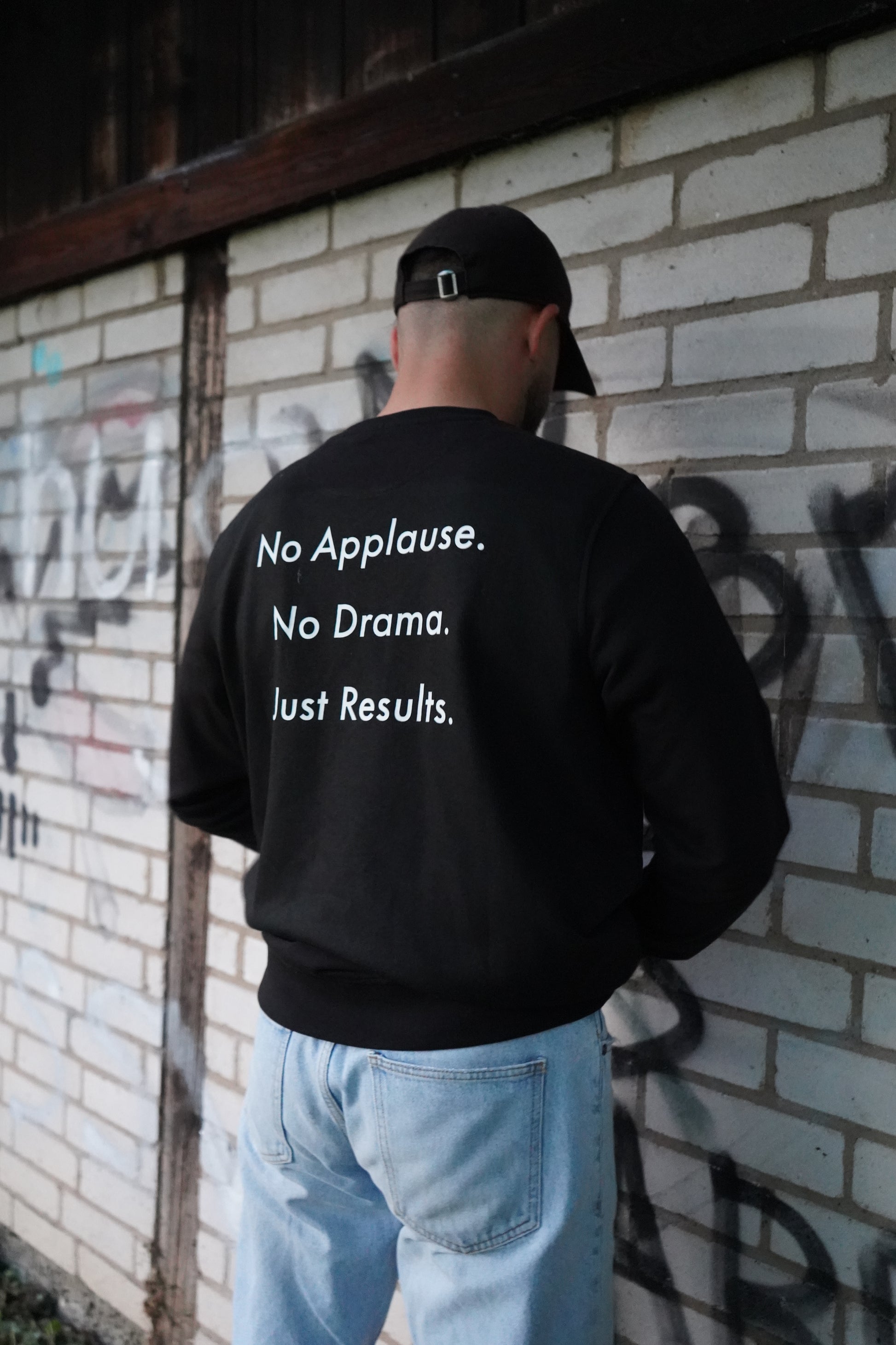 Echter Moment auf der Straße – Dunya-Lions-Sweater mit Rückenstatement vor Klinkerwand. Keine Show, nur Präsenz.